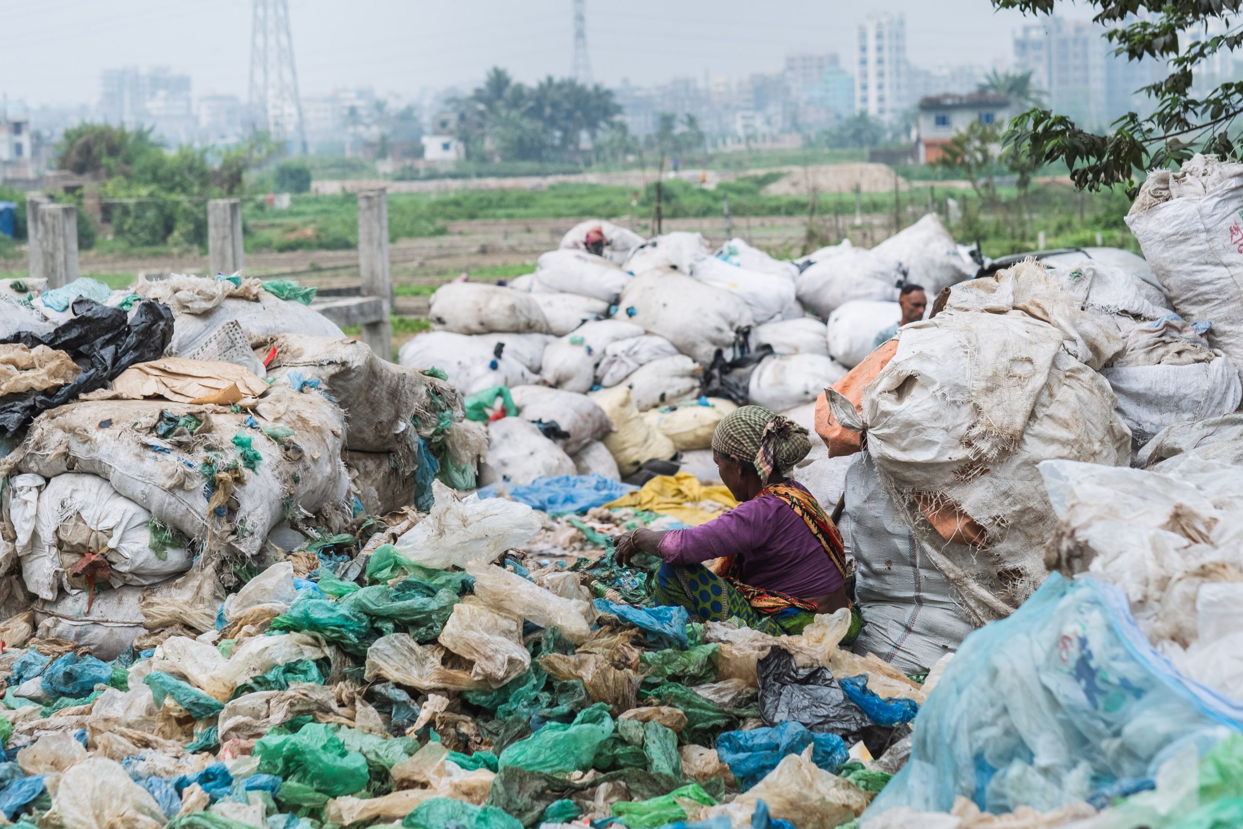 An image of a female presenting person in Dhaka dumpsite surrounding by bags of rubbish.